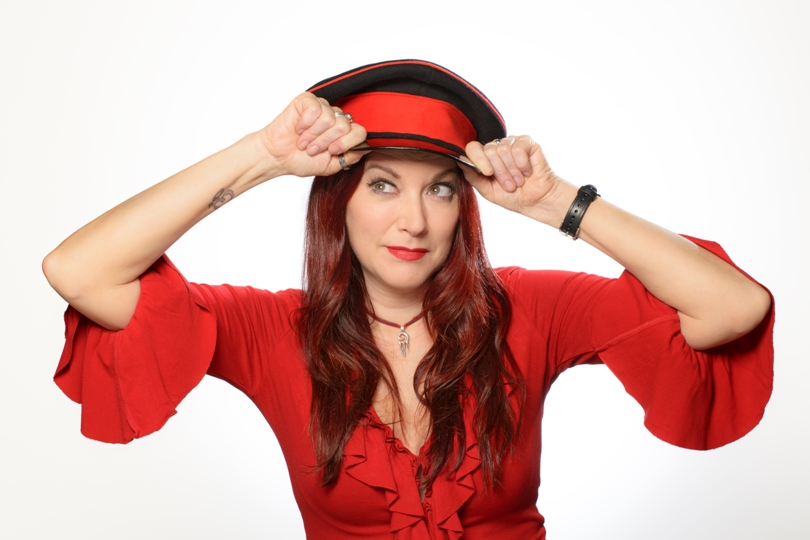 British female stand up comedian Susan Murray in a red dress with a peaked hat by Paul Tucker